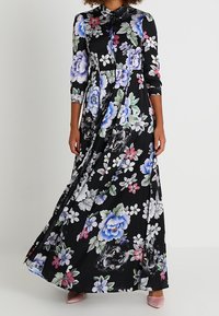 Robe maxi noire à fleurs avec manches longues, col et motifs floraux colorés en bleu, rose et vert. Texture de tissu lisse.