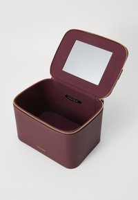 Maroon leather storage box with a rectangular shape, gold zipper, and an interior mirror on the lid; smooth texture and minimal branding.