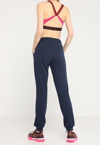 Marinblå joggingbyxor kombinerat med en vinröd och rosa sportbh. Outfiten har korsade axelremmar och slip-on sneakers med rosa sulor.