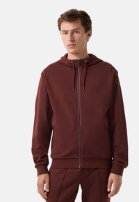 Bordeaux zip-up hoodie van zacht materiaal, met een capuchon, trekkoorden en geribbelde manchetten. Gecombineerd met bijpassende broeken.