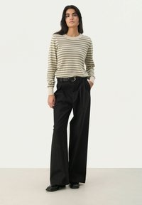 Raipe pullover-sweater beežis ja oliivrohelises, koos kõrge vöökohtadega mustade laia jalgadega pükstega, millel on ümmargune hõbedane pandla. 