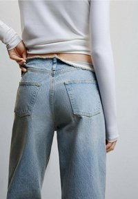 Jasnoniebieskie dżinsy z wysokim stanem, z postrzępionym paskiem i dwiema tylnymi kieszeniami. Tkanina ma miękką, zużytą teksturę.