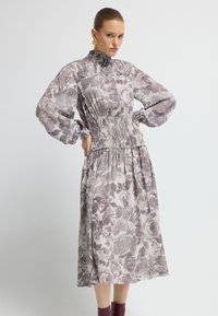 Vestido floral de manga larga en tejido suave, con cuello alto, cintura fruncida y falda fluida en tonos de púrpura y crema.