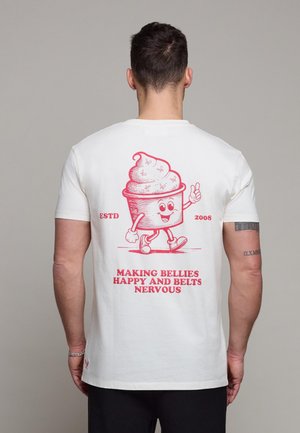 Mann iført hvit T-skjorte med rød tegneserieis-figur og teksten "Making bellies happy and belts nervous" på ryggen.