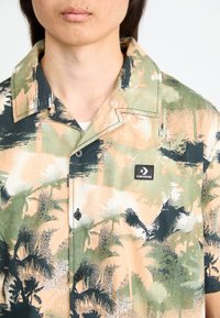 Korte mouw button-up shirt in pastelkleuren, met zwarte palmboomprints, groene accenten, subtiele texturen en een Converse logo label.