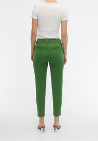 Pantalon vert slim avec une ceinture élastique, deux poches arrière, et une texture lisse, assorti à un T-shirt blanc uni.
