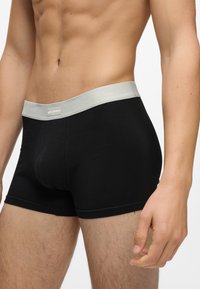 Chiloți boxer negri din bumbac, cu o talie elastică argintie netedă care poartă logo-ul brandului. Design simplu, fără modele sau accente vizibile.