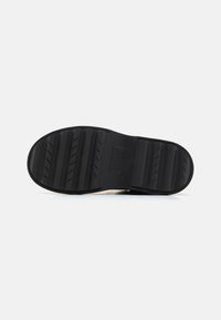 Suela de zapato de goma negra con ranuras y estrías profundas para tracción, marcada con el logo "GRIPPER" y detalles de tamaño. Forma plana y redonda.