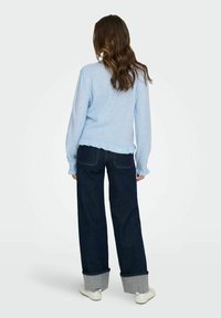 Ljusblått stickat tröja med scallopkant, parat med mörkblå vida jeans med ljusgrå manschetter och vita skor.