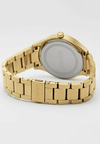 Orologio in metallo color oro con bracciale a maglie, cassa rotonda e retro circolare liscio. Presenta un nome di marca inciso sulla fibbia.