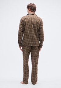 Braunes kariertes Pyjama-Set bestehend aus einem langärmligen, zum Knöpfen vorgesehenen Hemd und dazu passenden Hosen, beide mit kariertem Muster und weicher Textur.