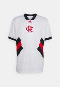 Maillot de soccer blanc avec des nervures horizontales, accents noirs sur les manches, et un logo rouge au centre avec des panneaux latéraux noirs et rouges.