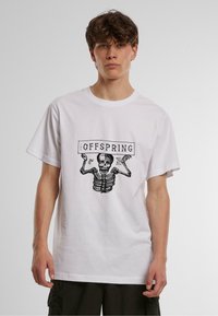 Valkoinen puuvillapaita, jossa on musta graafinen printti luurangosta, joka nostaa kylttiä, jossa lukee "THE OFFSPRING". Lyhyet hihat ja pyöreä kaula-aukko.