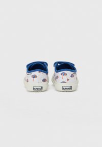 Tênis de lona com uma base branca, detalhes em azul e um padrão de guarda-sóis de praia multicoloridos. Apresenta uma sola de borracha e uma etiqueta logo na parte de trás.