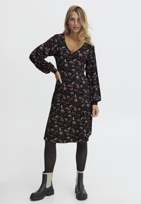 Langärmliges, schwarzes Kleid mit einem floralen Muster in verschiedenen Rosa-, Grün- und Weißtönen; hat einen V-Ausschnitt und eine lockere Passform.
