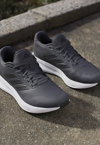 Le scarpe sportive grigie presentano una tomaia strutturata con un marchio a tre strisce tonali, una suola bianca imbottita e un design con lacci.