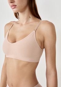 Bralette de color rosa claro, hecho de un material suave y elástico, con tirantes ajustables, forma de triángulo y una banda sin costuras bajo el busto.
