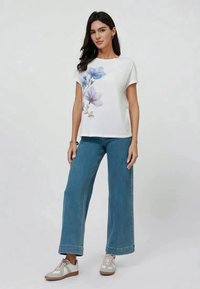 Hvid bomulds-T-shirt med print af blå blomster på forsiden, kombineret med viddebenet denim jeans og beige sneakers. Minimalistisk design.