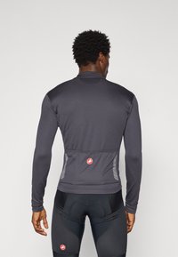 Maillot de cyclisme à manches longues, près du corps, en gris foncé avec un tissu texturé, des accents réfléchissants et un design ergonomique. Présente un logo dans le dos.