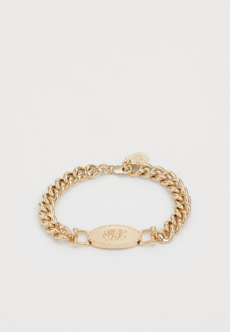 Zelta metāla ķēdes aproce ar ovālu piekariņu, uz kura ir iegravēti burti. Aprocei ir gludas saites un āķa aizdare.