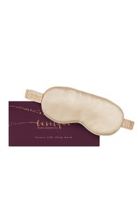 Beige zijden slaapmasker met elastisch bandje liggend op een paarse doos met label "le silque pure moments luxury silk sleep mask."