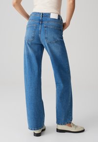 Jeans de mezclilla azul de pierna ancha con cintura alta, corte recto y dos bolsillos traseros. La tela tiene una textura suave con un desvanecido mínimo.