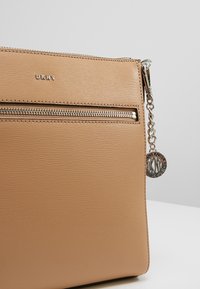 Borsa a tracolla in similpelle beige con superficie testurizzata, zip argentata e dettaglio in catena con ciondolo rotondo del logo.