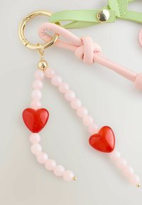 Llavero con un anillo dorado, correas en rosa y verde, y una cadena de cuentas con cuentas rosas y dos acentos en forma de corazón rojo.