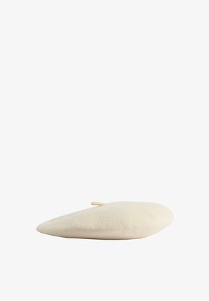 Beżowy wełniany beret z małym ogonkiem na górze, przedstawiony na białym tle.