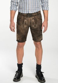 Braune Ledershorts mit dekorativer Stickerei, strukturiertem Finish und Knopfakzenten. Kombiniert mit einem karierten Hemd und schwarzen Schuhen.