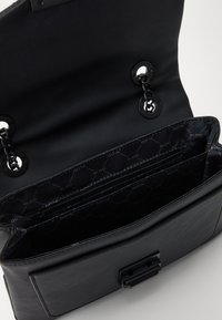 Borsa a mano in pelle nera con superficie testurizzata, dotata di tracolla a catena e più scomparti, tra cui una tasca con zip.