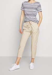 T-shirt à manches courtes rayé bleu marine et blanc, associé à un pantalon cargo beige avec taille élastique. Le mannequin porte des baskets blanches.