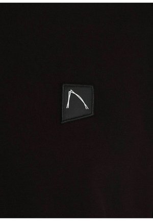 Zwarte stof met een zachte textuur heeft een klein, zwart patch met een wit geometrisch logo. Het ontwerp is minimalistisch en modern.
