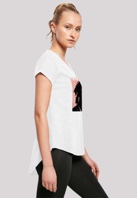 White, short-sleeve t-shirt with a relaxed fit. Features a large black and pink graphic on the front. The back is slightly longer than the front.