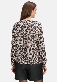 Sweter w wzór lamparta z miękkiego materiału, z długimi rękawami, o okrągłym dole i ściągaczach na mankietach. Nosi się go na czarnych skórzanych szortach.