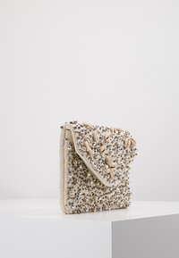 Beadad kuvertväska med beige tyg och silver- samt krämfärgade dekorationer, en klaffstängning och en texturerad yta.