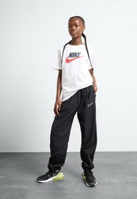 White Nike t-shirt with red and black logo, paired with black athletic pants featuring a small white logo and black/green Nike sneakers.