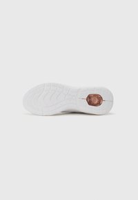 Hvite sneakersåler med teksturert grepemønster og en sentral bronseakent. Glatt materiale og avrundet form for komfort.
