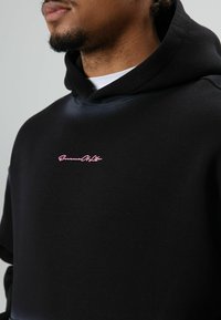 Zwarte hoodie van een zachte katoenmix met een roze geborduurd logo op de borst. Ontworpen met een ontspannen pasvorm en zonder zichtbare patronen.