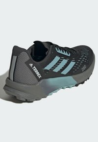 Scarpa atletica nera e azzurra chiara con tomaia in mesh testurizzato, design con tre strisce prominenti e suola grigia robusta per la trazione.