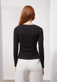 Svart langermet topp med rund hals, slim fit, og glatt tekstur. Kombinert med hvite vide bukser. Minimalistisk design uten mønstre.