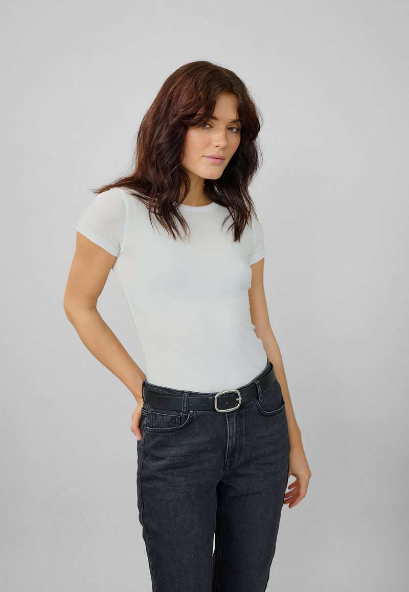 T-shirt bianco attillato con maniche corte, abbinato a jeans scuri a vita alta e una cintura nera con fibbia argentata.