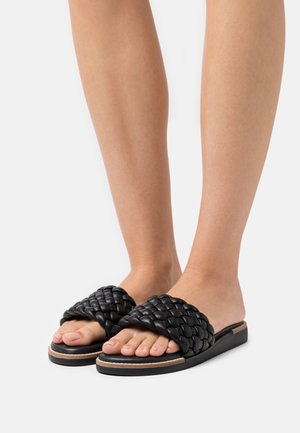 Sandales glissantes noires en tissu tressé avec une tige épaisse, semelle plate et couture contrastante beige. Le design à bout ouvert met en valeur les orteils.