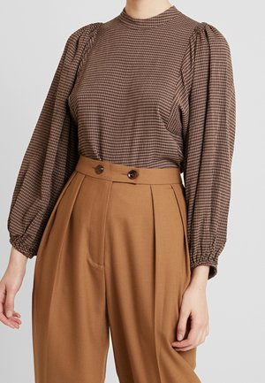 Brun ternet bluse med lange ærmer og puffede ærmer, stylet med camel-farvede bukser med høj talje og knapdetaljer.