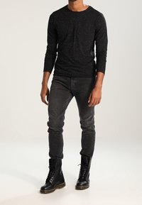 Czarna koszula z długim rękawem w nakrapiany wzór, zestawiona z ciemnoszarymi jeansami slim fit i czarnymi botkami wojskowymi na sznurówki.