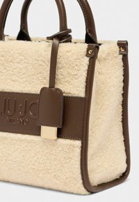 Sac en fausse fourrure crème avec des accents en cuir marron, doté de petites poignées, d'une plaque logo et de détails en métal doré.