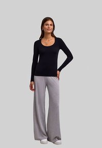 Zwart top met lange mouwen en een ronde hals, gecombineerd met lichtgrijze broek met wijde pijpen en witte sneakers. Glad materiaal, eenvoudig ontwerp.