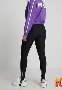 Purple cropped jacket with white stripes, paired with black ribbed leggings featuring "PUMA" branding and purple-accented sneakers.