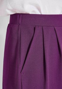 Hooggewaisted paarse rok met plooien en een zijzak, gecombineerd met een witte top die erin gestopt is.