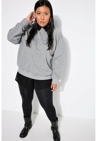 Felpa grigia oversize, pantaloni corti neri a righe, leggings neri con dettagli in perle e stivaletti neri. Tessuto morbido e vestibilità comoda.